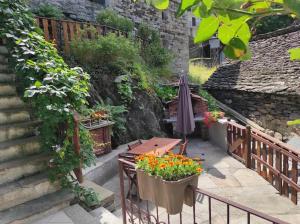 a patio with a table and an umbrella and flowers at CASA DEL CIOS calda e intima casetta immersa nel verde delle montagne in Alpe Basciumo