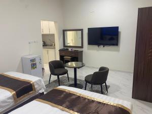 Cette chambre comprend 2 lits, une table et une télévision. dans l'établissement Wind alula, à Al-Ula