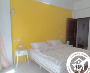 um quarto com uma cama com uma parede amarela em 東津左岸民宿 em Yilan City