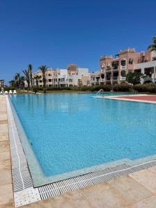 een groot blauw zwembad met gebouwen op de achtergrond bij Appartement en résidence + grande terrasse sur le toit in Saidia 