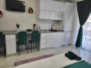 a kitchen with white cabinets and a table with green chairs at Garsoniera Ady in Mangalia