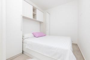 a white bedroom with a bed and a purple pillow at Apartments Tony in Mali Lošinj