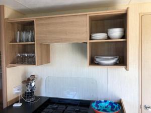 a kitchen with wooden cabinets with plates and dishes at Meadow View Horizon Static Caravan in Barnstaple