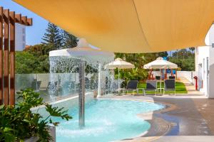 a fountain in a pool with chairs and umbrellas at NissiBlu Beach Resort in Ayia Napa