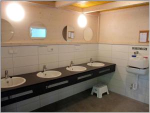 a bathroom with three sinks and a toilet and mirrors at Baumzeltdorf OSTSEEBREEZE direkt am Strand in Dranske