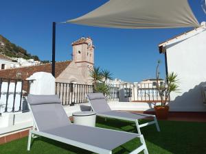 two chairs and a table on a balcony with a clock tower at Casa Sarasvati in Frigiliana