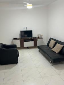 a living room with a black couch and a tv at NOVO pitangueiras service 2, dois dormitórios, 100 m da praia, duas vagas de garagem, completo in Guarujá
