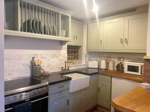 a kitchen with white cabinets and a sink and a stove at Carpenters Cottage Quirky home Seaside town in Minehead