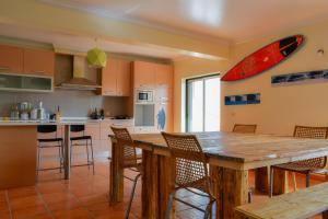 een keuken met een houten tafel met stoelen en een surfplank aan de muur bij Mayla Surf House in Aljezur