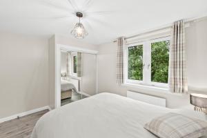 a white bedroom with a bed and two windows at The Riverside Rest in Stirling