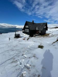 a black house in the snow with footprints in front at Unique and isolated cottage with stunning views in Leynar