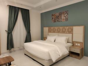 a bedroom with a large white bed with green curtains at Kyan Park Abha Hotel in Abha