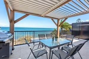 eine Terrasse mit einem Tisch, Stühlen und Meerblick in der Unterkunft Bay Vista Two Bedroom Waterfront Apartment in Redcliffe