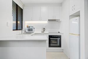 eine weiße Küche mit weißen Schränken und einem Kühlschrank in der Unterkunft Manuka Park Serviced Apartments in Canberra