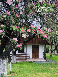 ein kleines Gebäude mit einer Bank und rosa Blumen in der Unterkunft Еко Дім з СОЛОМИ in Solotschyn