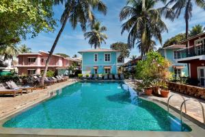 a swimming pool in front of a house with palm trees at Aldeia Santa Rita - Candolim in Candolim