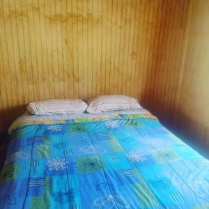 a bed with a blue comforter and white pillows at Cabaña bellavista in Cochamó