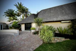 a house with a thatched roof and some palm trees at Decollage Estate in Polokwane