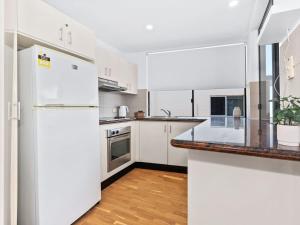 a kitchen with white cabinets and a white refrigerator at Beached On Marine Parade in Kingscliff
