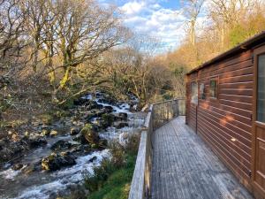 een houten loopbrug naast een rivier naast een huis bij Snowdonia Holiday Lodges in Beddgelert