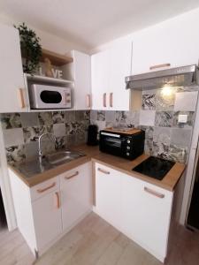 a kitchen with white cabinets and a sink and a microwave at Appartement Zen à Frejus avec jardin, piscine, tennis, proche mer in Fréjus