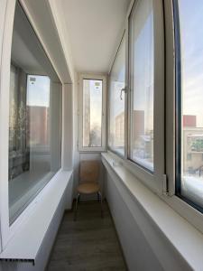 Habitación con 2 ventanas y silla. en VIP квартира в Центре, 2 комнаты, en Kostanái