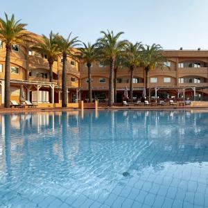 une grande piscine avec des palmiers en face d'un bâtiment dans l'établissement Reggio Calabria Altafiumara Resort & Spa, à Villa San Giovanni