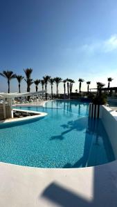 a large swimming pool with palm trees in the background at Riviera Hotel and Beach Lounge, Beirut in Beirut