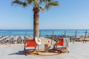 two chairs and a palm tree on the beach at Aquila Porto Rethymno in Rethymno