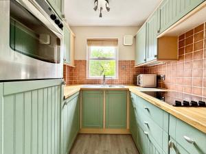 eine Küche mit grünen Schränken und einem Fenster in der Unterkunft Cherry Blossom Cottage in York + 23 Fotos
