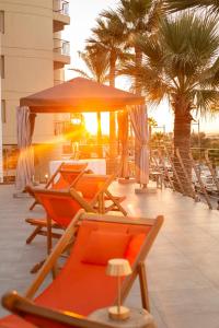 a deck with chairs and an umbrella and palm trees at Aquila Porto Rethymno in Rethymno Town
