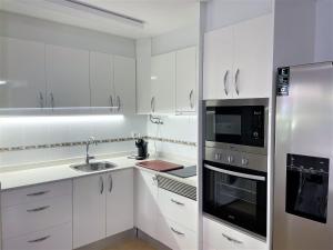 Una cocina con gabinetes blancos y un refrigerador de acero inoxidable. en Edison Bungalow LEK con aire, en Peñíscola