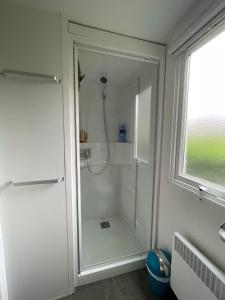 La salle de bains est pourvue d'une douche blanche et d'une fenêtre. dans l'établissement Mobil-home Clim, Tv, Lv - Camping Lac des Rêves 4 étoiles - 010, à Lattes