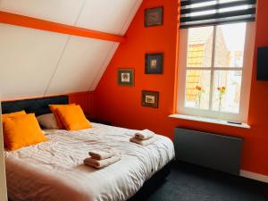 a bedroom with orange walls and a bed with towels on it at B&B with or without De Schuur in Zierikzee