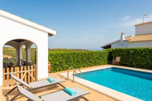 a swimming pool with two lounge chairs next to a house at Villa Cala Llonga in Mahón