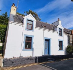 a white house with a dog in the window at The Portpatrick Pad - A cosy 3 bed cottage, w. sea views & garden office in Portpatrick