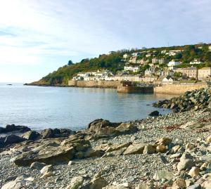 a rocky beach with houses on a hill next to the water at The Seawitch - harbourside apartment in Mousehole