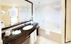ein Badezimmer mit Waschbecken, Badewanne und Spiegel in der Unterkunft Dorint An der Messe Köln in Köln