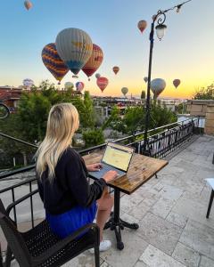 uma mulher sentada numa mesa com um computador portátil numa varanda com balões em Nomads Cave Hotel & Rooftop em Goreme