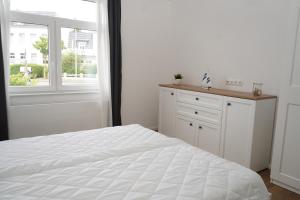 ein weißes Schlafzimmer mit einem weißen Bett und einem Fenster in der Unterkunft Strandhaus Döse 1 in Cuxhaven