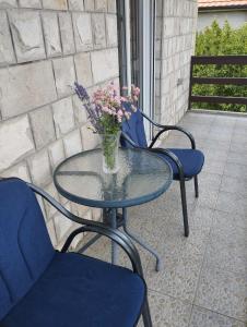 a glass table and two chairs with a vase of flowers at Apartman Petar in Trebinje