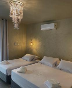 two beds in a bedroom with a chandelier at Pousada Ybitu in São Miguel do Gostoso