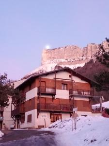a building in the snow with a mountain in the background at Appartement des cimes du Granier in Les Déserts