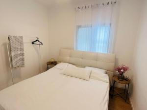 ein weißes Bett in einem Zimmer mit Fenster in der Unterkunft פינה בשחף in Bustan HaGalil