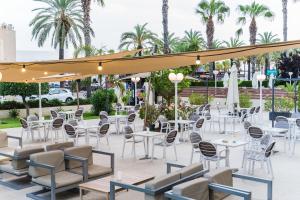 un patio con mesas blancas, sillas y palmeras en Hotel Planas, en Salou