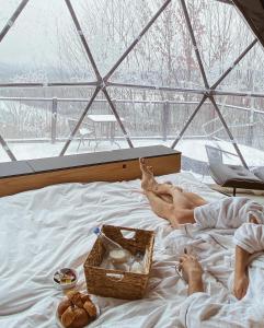 two people laying on a bed with a basket of food at Bel Air Tremblant Hotel & Residences in Mont-Tremblant