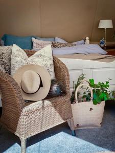 un sombrero de paja sentado en una silla de mimbre junto a una cama en Idyllisk glamping rett ved elven, en Skien