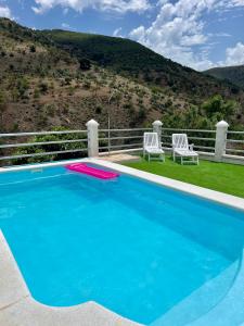 a blue swimming pool with two chairs and a fence at Casa rural Las Casillas in Málaga