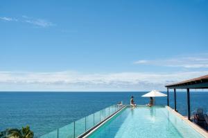 two people sitting on the edge of a swimming pool overlooking the ocean at Hotel Basalto in Punta Mita