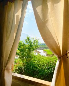 a window with a curtain with a view of a field at maison Rose & Jardinier eco homestay in Sa Pả